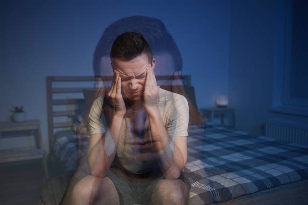 anxious man with headache sitting in bedroom with head in hands.